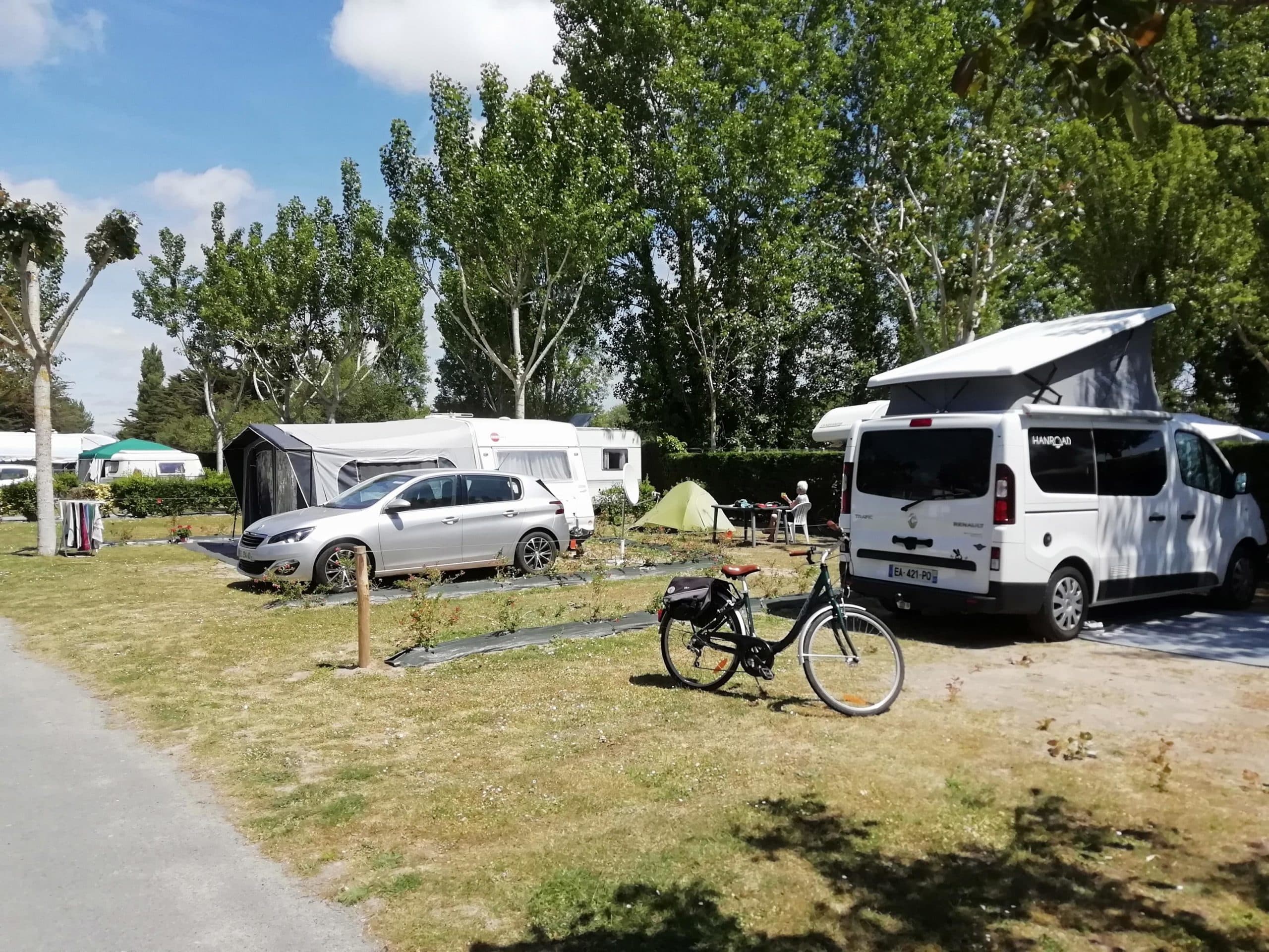 Camping avec caravanes, tente, bicyclette et arbres.
