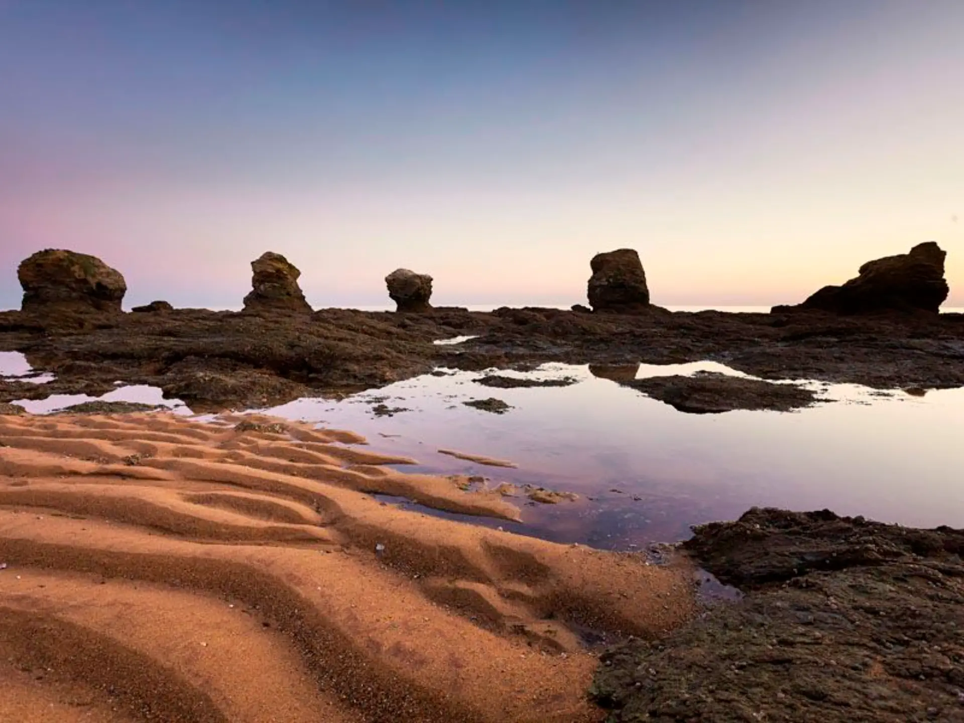Plage rocheuse au lever du soleil, sable ondulé.
