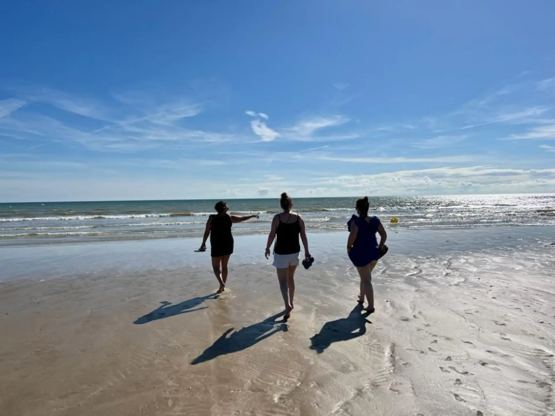 Trois personnes marchent sur une plage ensoleillée.