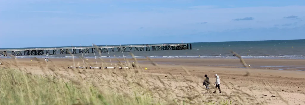 Plage avec jetée en arrière-plan et promeneurs