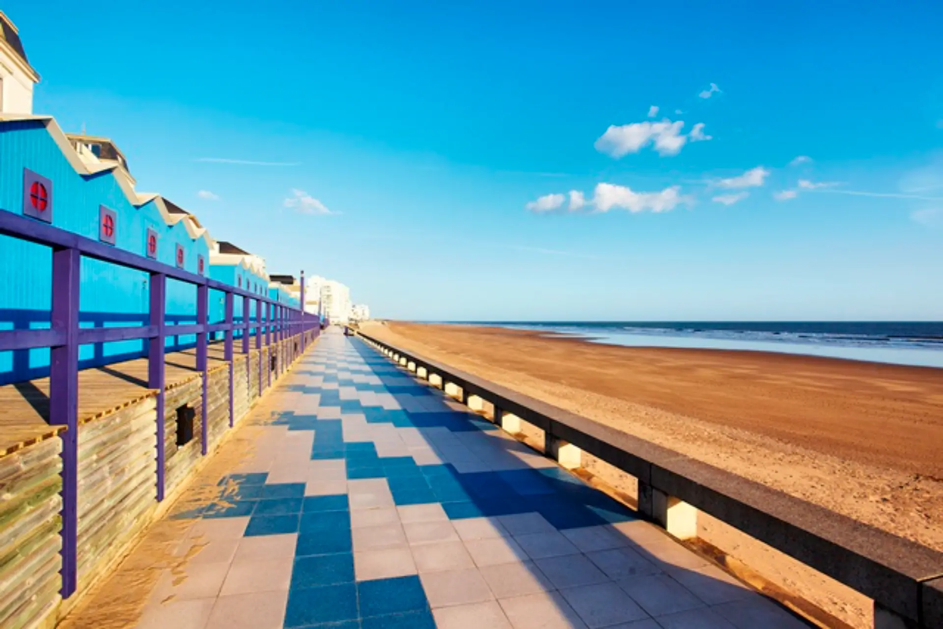 Promenade côtière avec cabines bleues et plage.