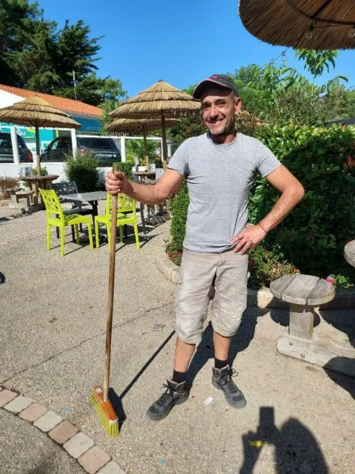 Homme souriant avec balai dans un jardin.