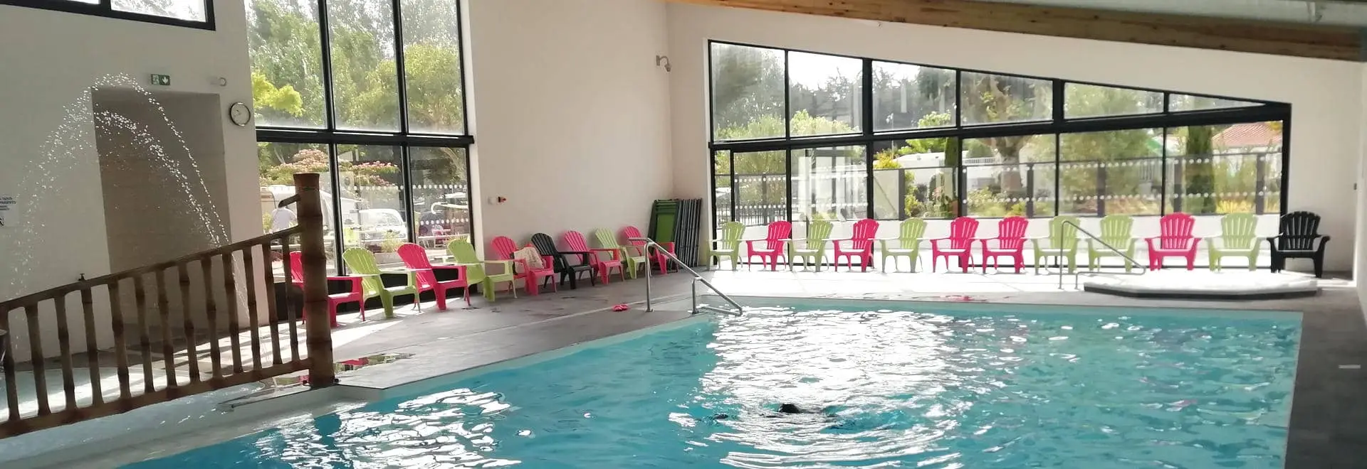Piscine intérieure avec chaises colorées autour.
