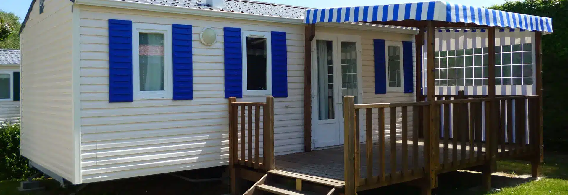 Mobil-home avec terrasse en bois et auvent rayé.