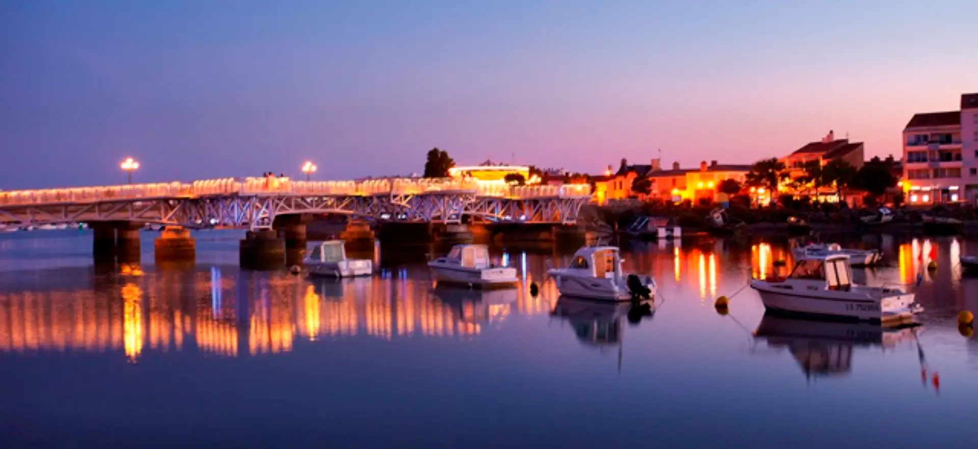 Pont illuminé au crépuscule avec bateaux amarrés.