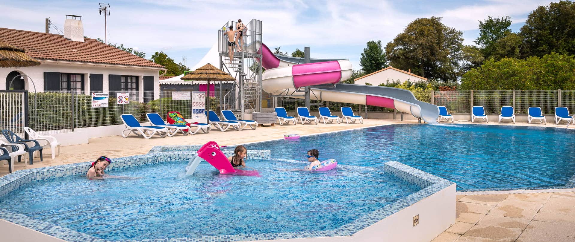 Piscine extérieure avec toboggan et transats bleus.